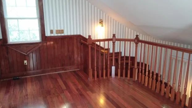 Loft interior with hardwood floors, wood paneling, staircase, and a window with natural light.