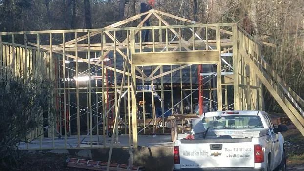 Wooden building under construction; truck parked in front, person on top of frame.