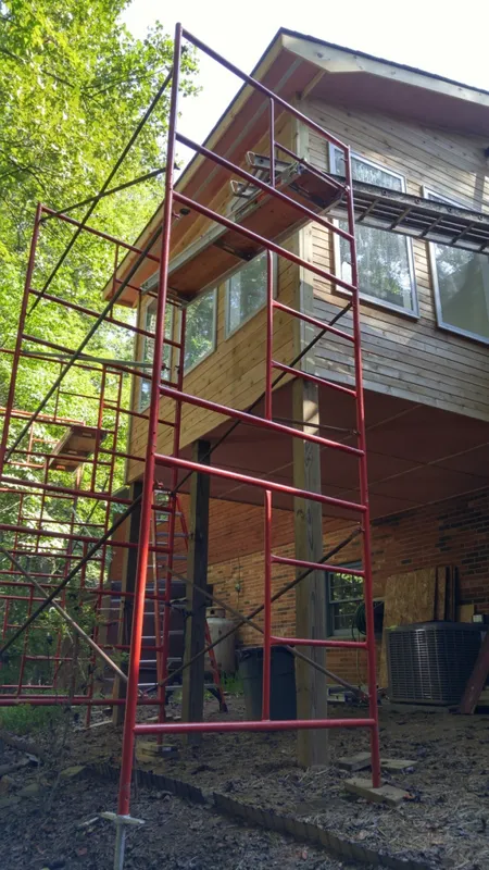 Red scaffolding next to a wooden building under construction.
