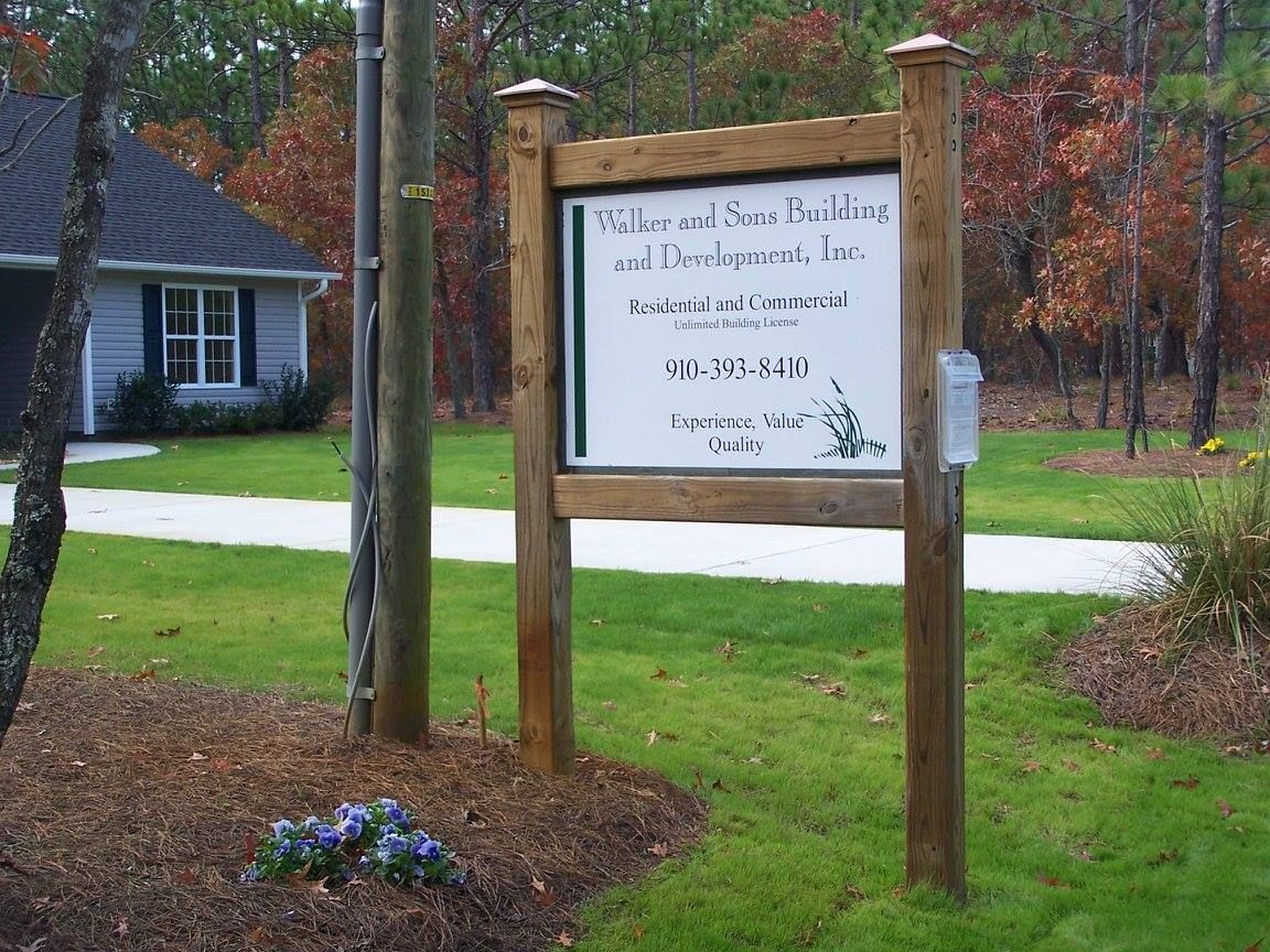 Wooden sign for Williams and Stone Building & Development, Inc. in front of a building with a blue facade and a green lawn.