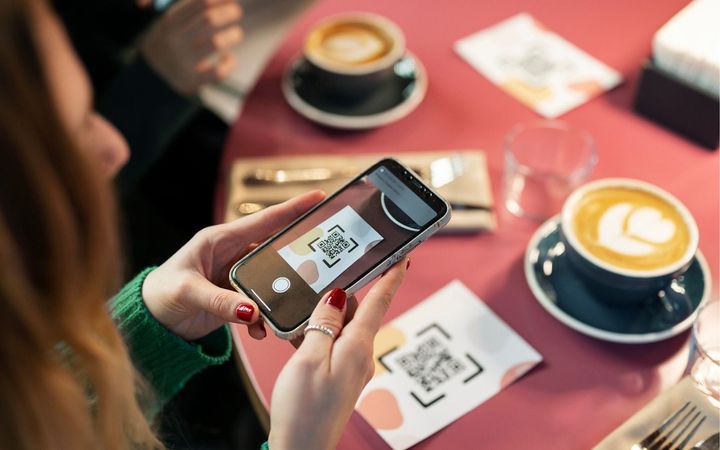 A woman is sitting at a table using a cell phone to scan a qr code.