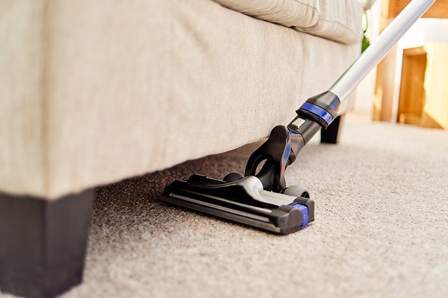 A Vacuum Cleaner is Sitting Under a couch in a Living room — Coffs Carpet Cleaning in Coffs Harbour, NSW