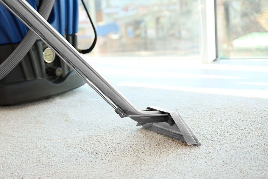A Vacuum Cleaner is Cleaning a Carpet in a Room — Coffs Carpet Cleaning in Coffs Harbour, NSW