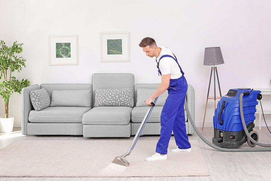A Man is Cleaning a Carpet with a Vacuum Cleaner in a Living Room — Coffs Carpet Cleaning in Coffs Harbour, NSW