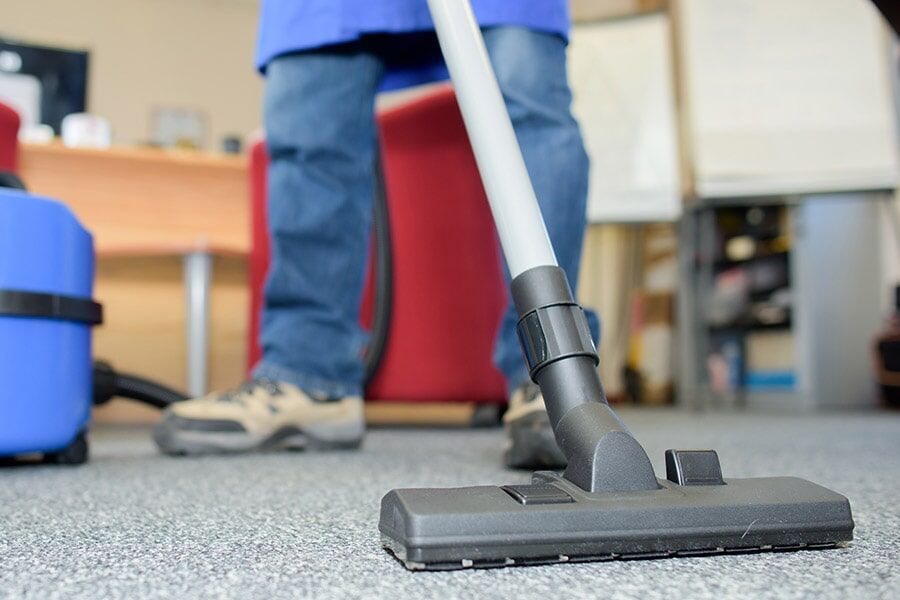 A Person is Using a Vacuum Cleaner to Clean a Carpet in an Office — Coffs Carpet Cleaning in Coffs Harbour, NSW