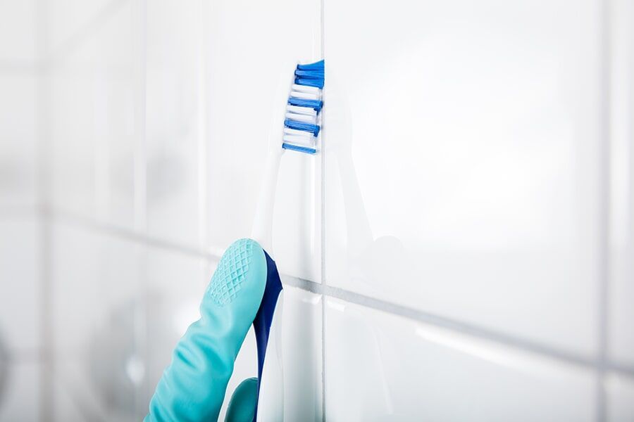 A Person is Cleaning a Tile Wall With a Toothbrush — Coffs Carpet Cleaning in Coffs Harbour, NSW