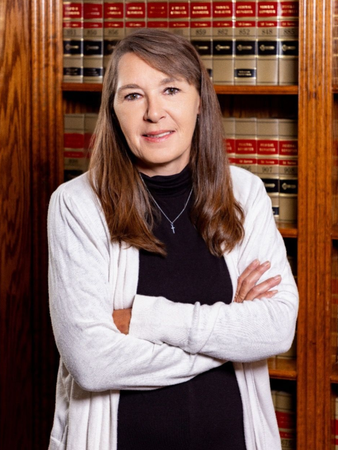 Woman in a white cardigan and black top, arms crossed, smiling, in front of a bookcase.