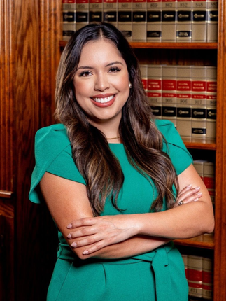 Woman with crossed arms smiles in front of a bookshelf, wearing a green dress.