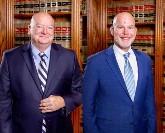 Two men in suits standing in front of a bookcase, smiling.