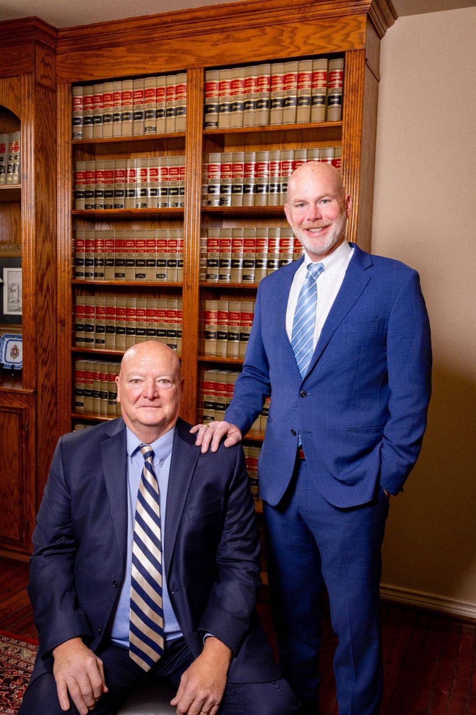 Two men in suits pose in front of a bookcase filled with law books.