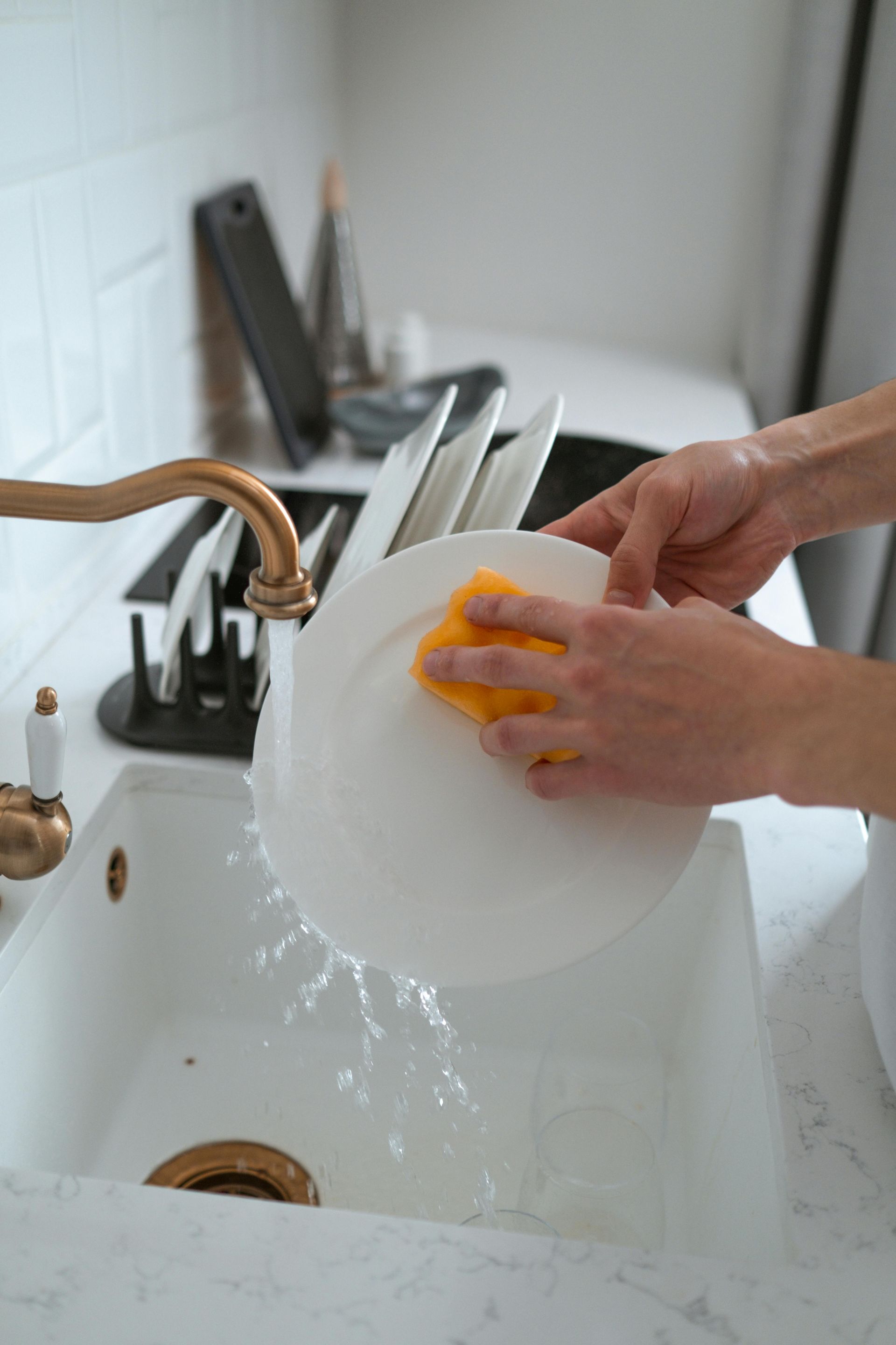 A person is washing a plate in a kitchen sink with a sponge.