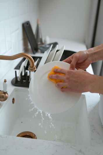 A person is washing a plate in a kitchen sink with a sponge.