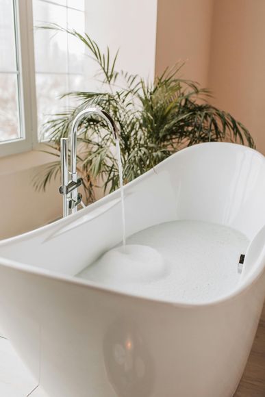 A white bathtub is filled with water in a bathroom next to a window.