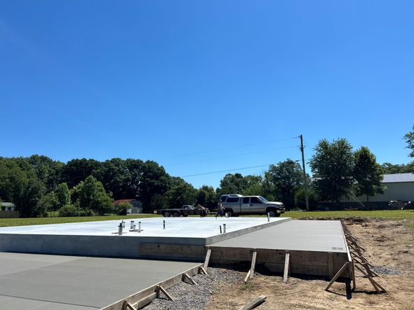 Concrete pad under construction beside a road, with workers and a white pickup on a sunny day