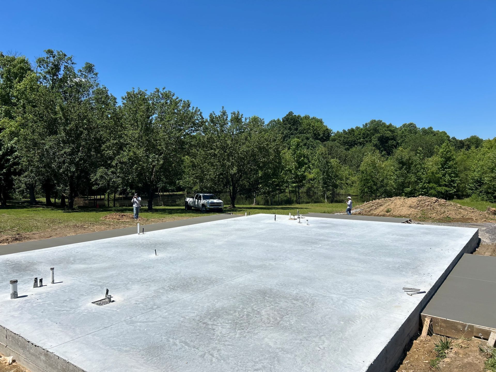 Fresh concrete slab at a construction site beside trees and a blue sky