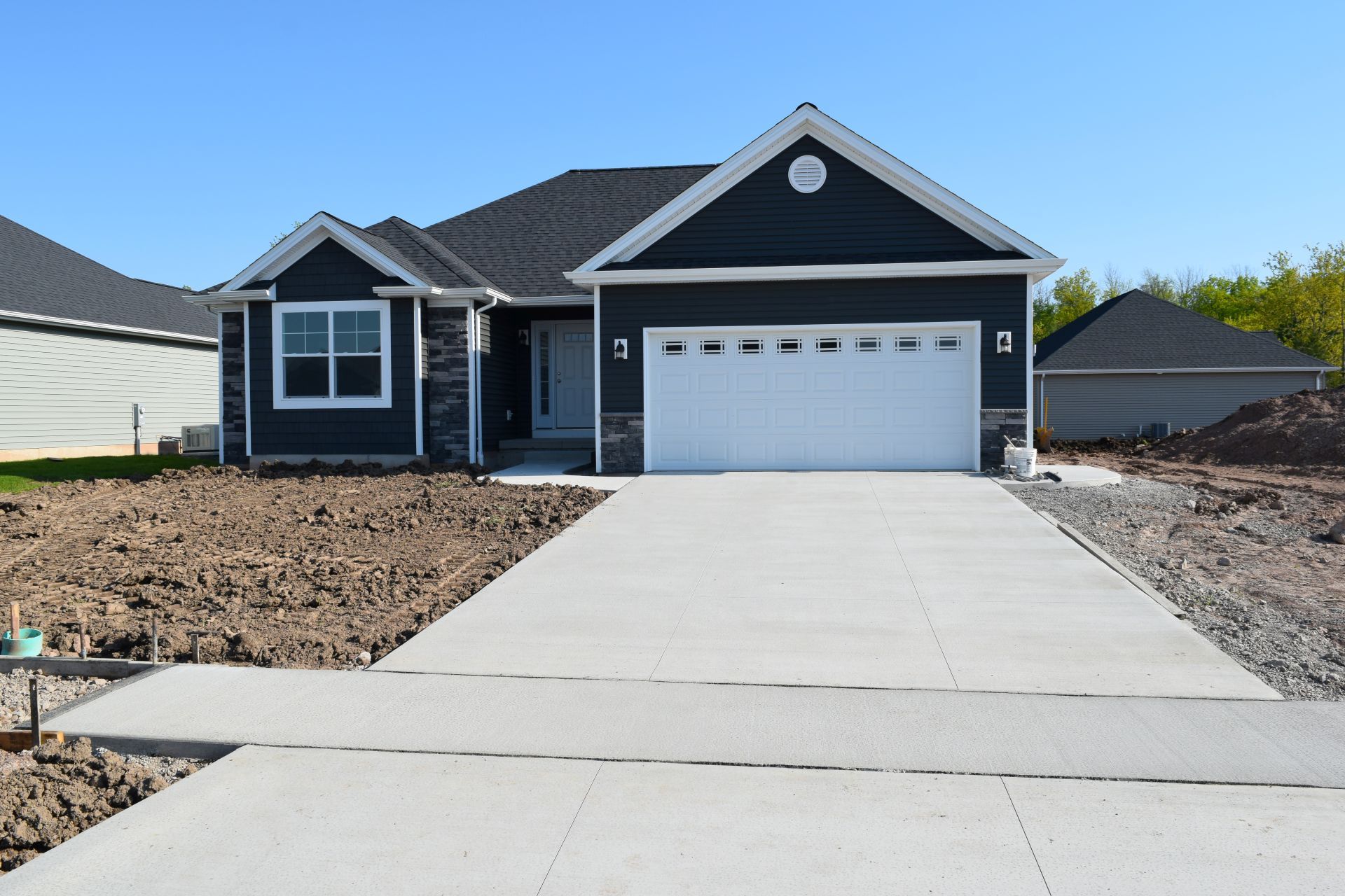 Single-story house with dark siding, white garage, and a long concrete driveway under clear blue sky