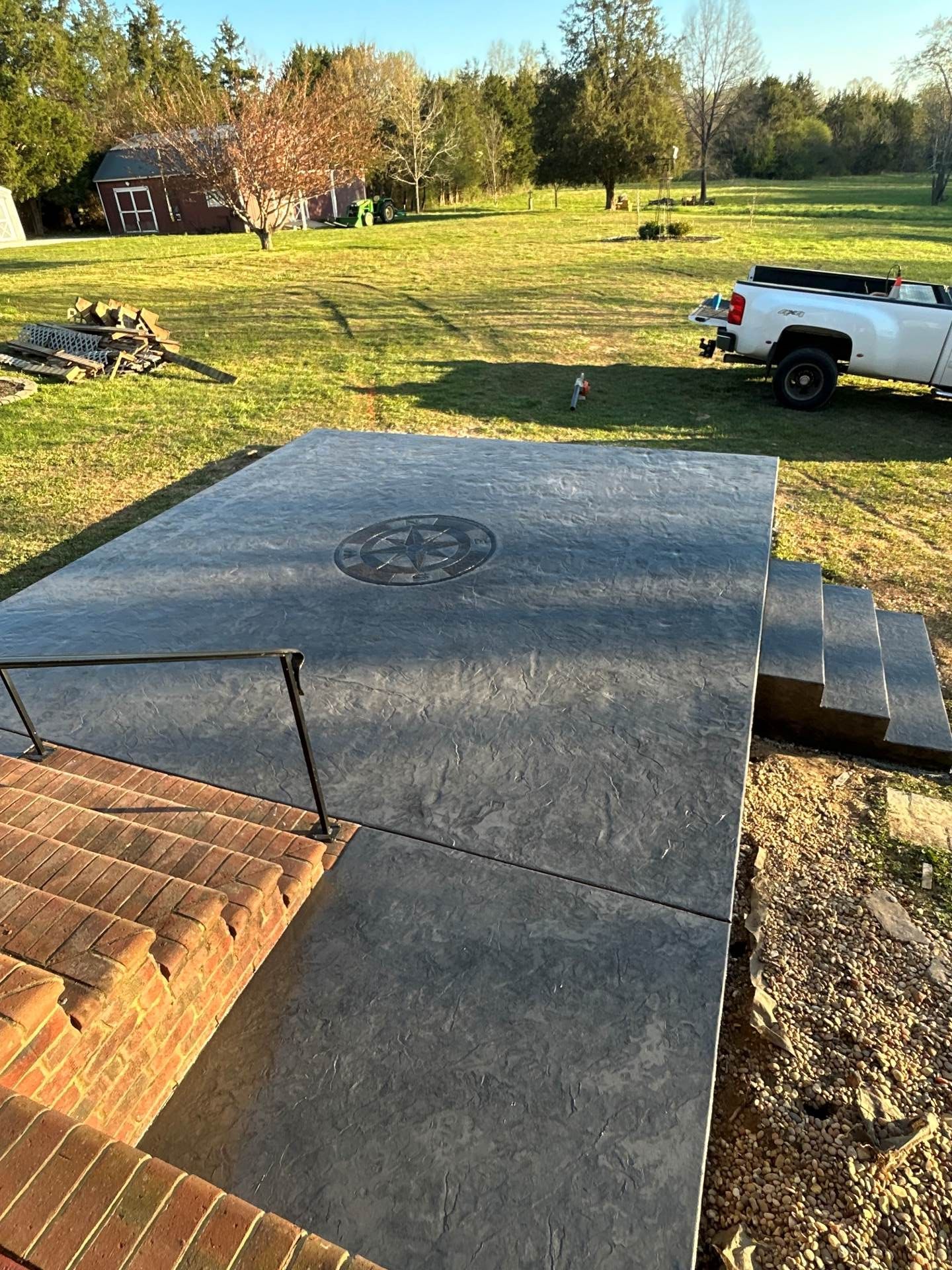 Stone patio in a grassy yard with a white pickup truck, steps, and trees in the background