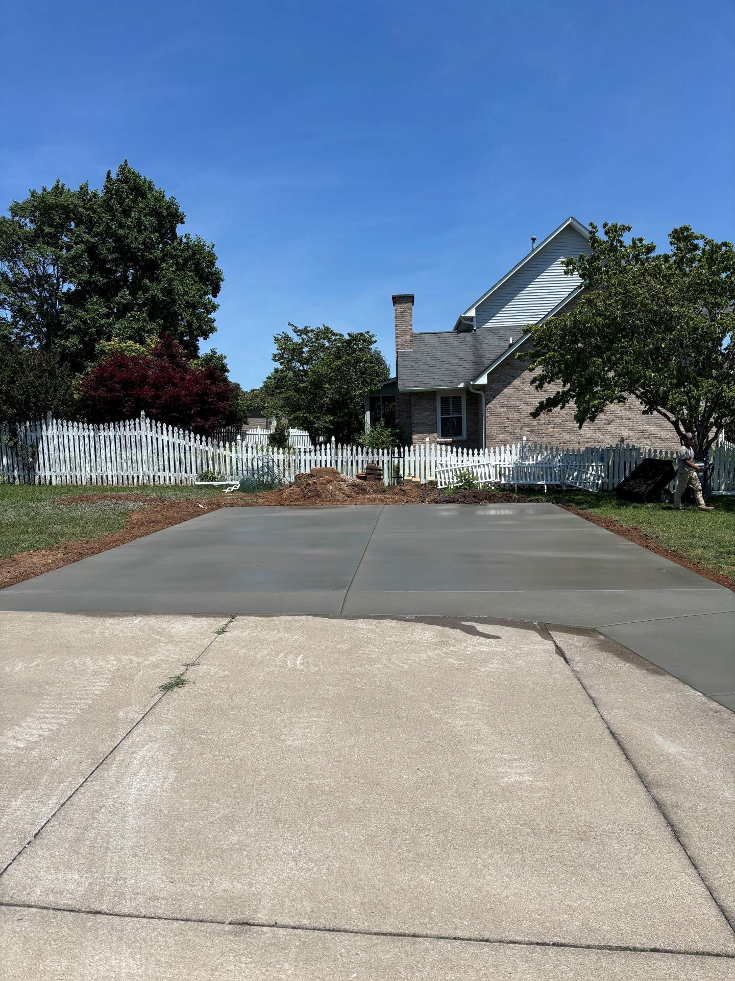 Driveway leading to a house with a white fence, trees, and a clear blue sky