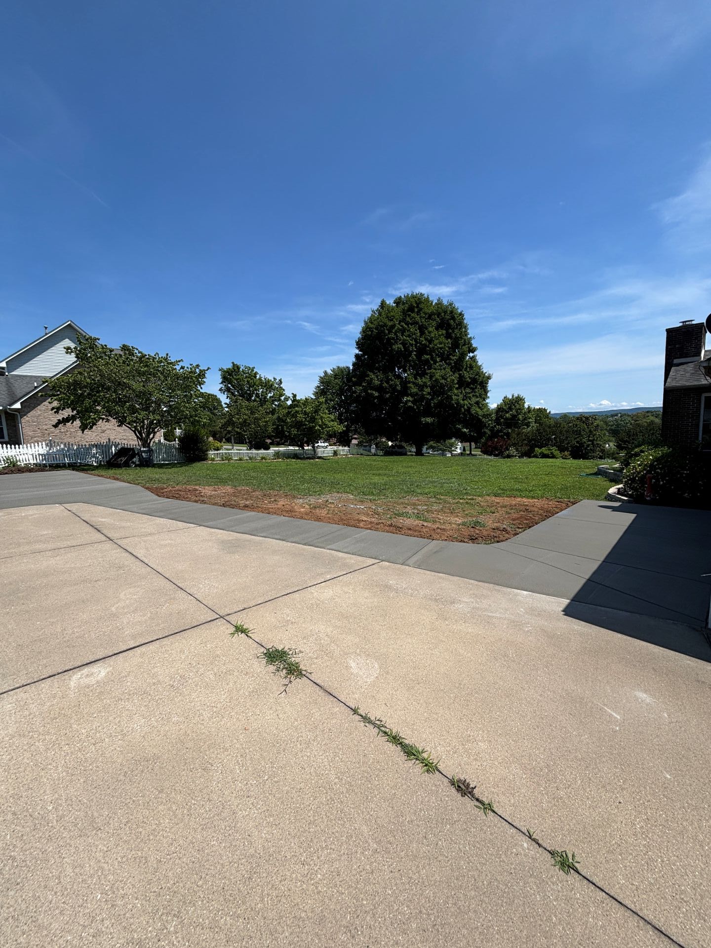 Quiet suburban driveway beside a grassy lot under a clear blue sky