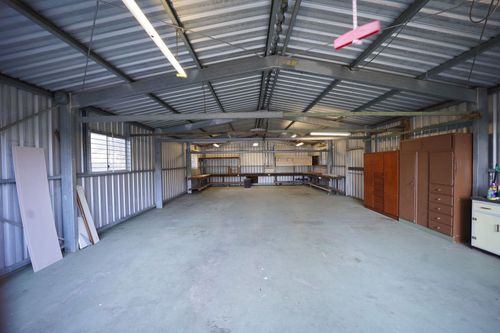 Empty metal warehouse interior with concrete floor, exposed beams, and shelves along the back wall