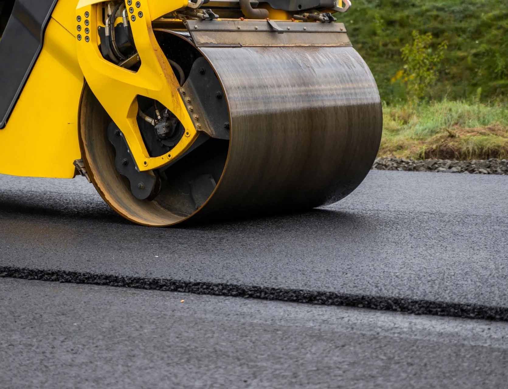 Un rouleau jaune déroule l'asphalte sur une route.
