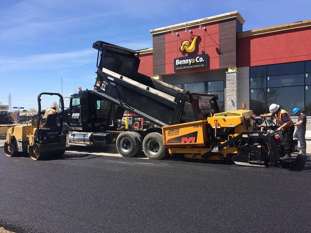 Un camion-benne est chargé d'asphalte devant un immeuble.