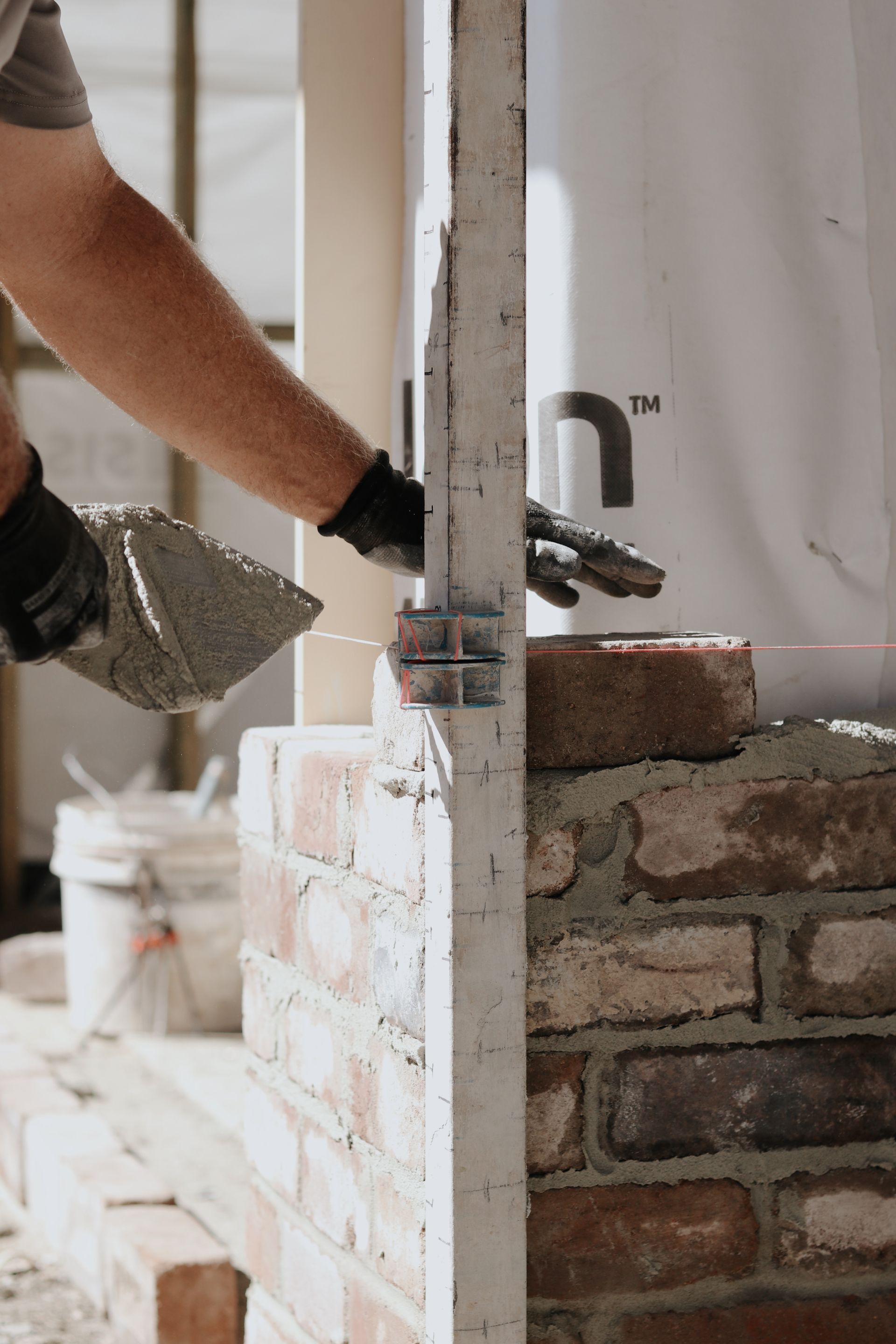 A Person Laying Bricks on a Wall, Using a Trowel and Level, Outdoors — Ryan's Bricklaying In Maitland, NSW