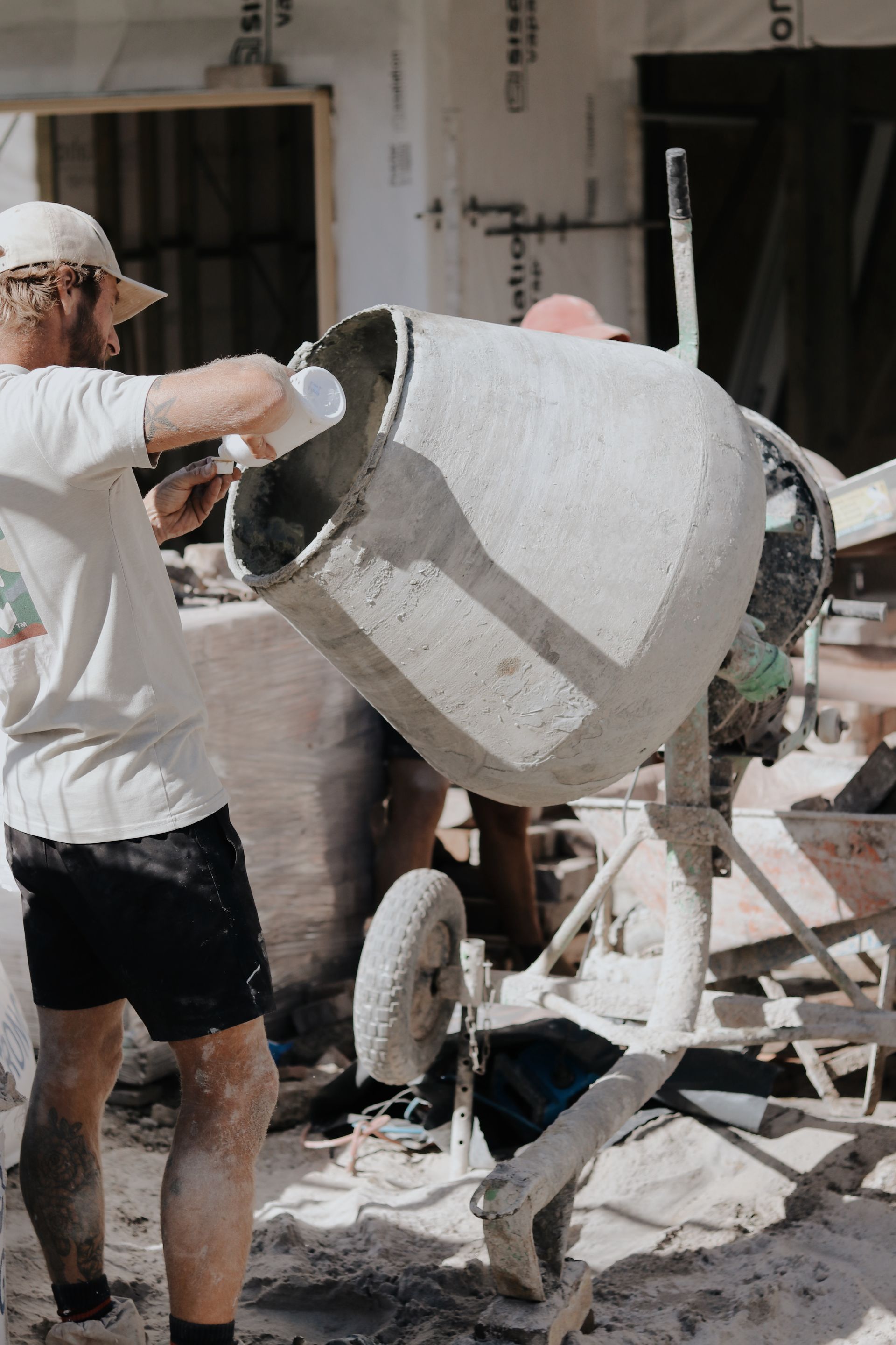 Man Pouring From a White Container Into a Concrete Mixer — Ryan's Bricklaying In Eleebana, NSW