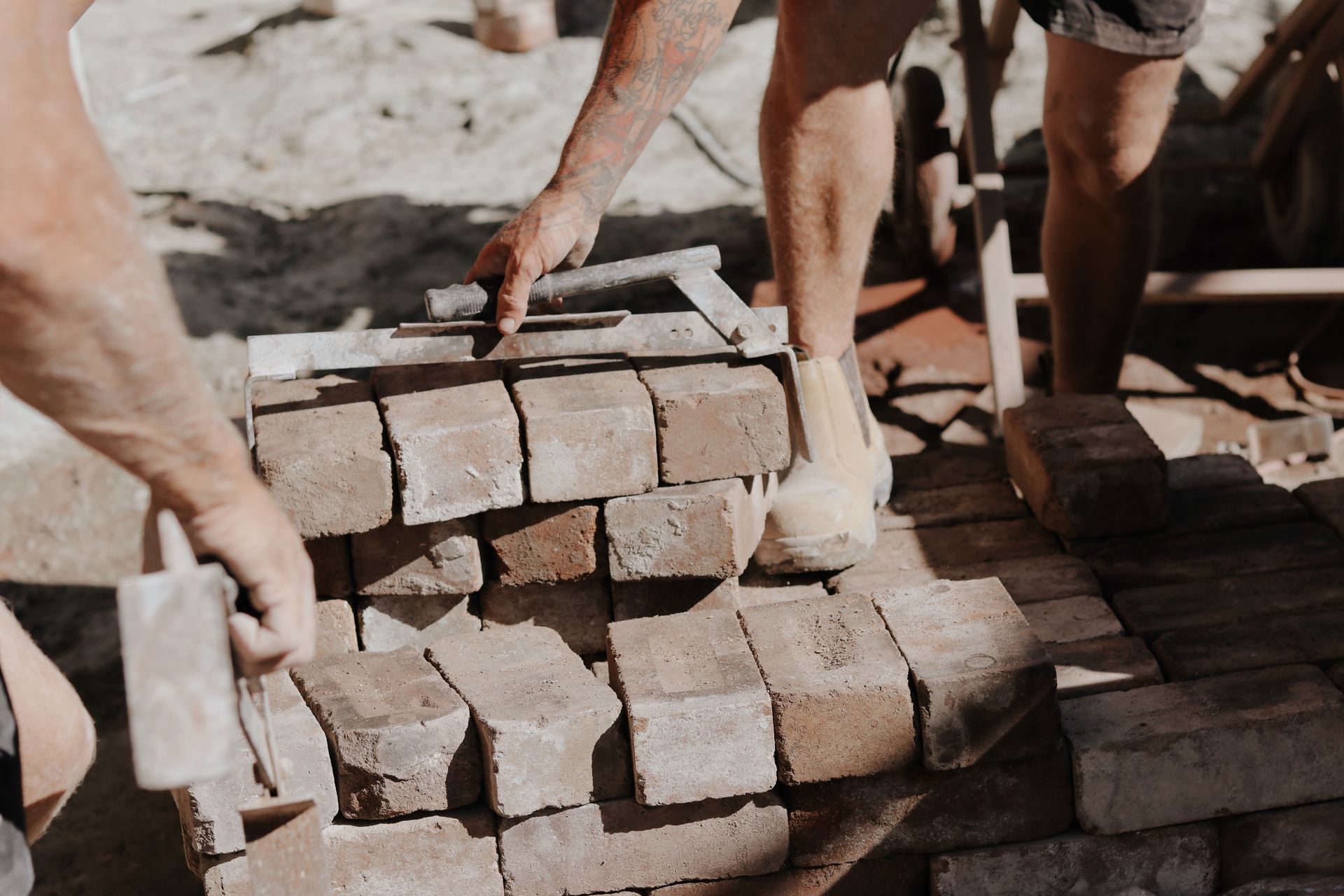 Two people laying bricks on a sandy surface. One uses a tool to level, the other places a brick— Ryan's Bricklaying In Eleebana, NSW