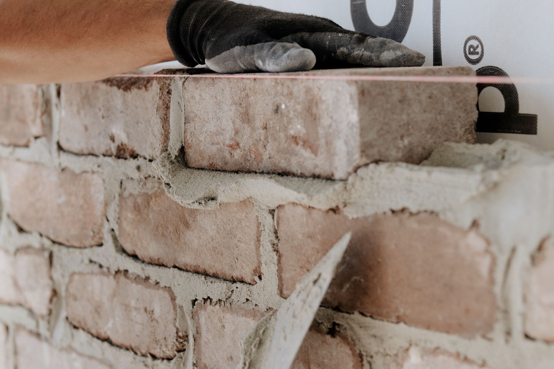 Gloved hand working with brick and mortar, applying mortar to brick. Pink string guides the alignment— Ryan's Bricklaying In Eleebana, NSW