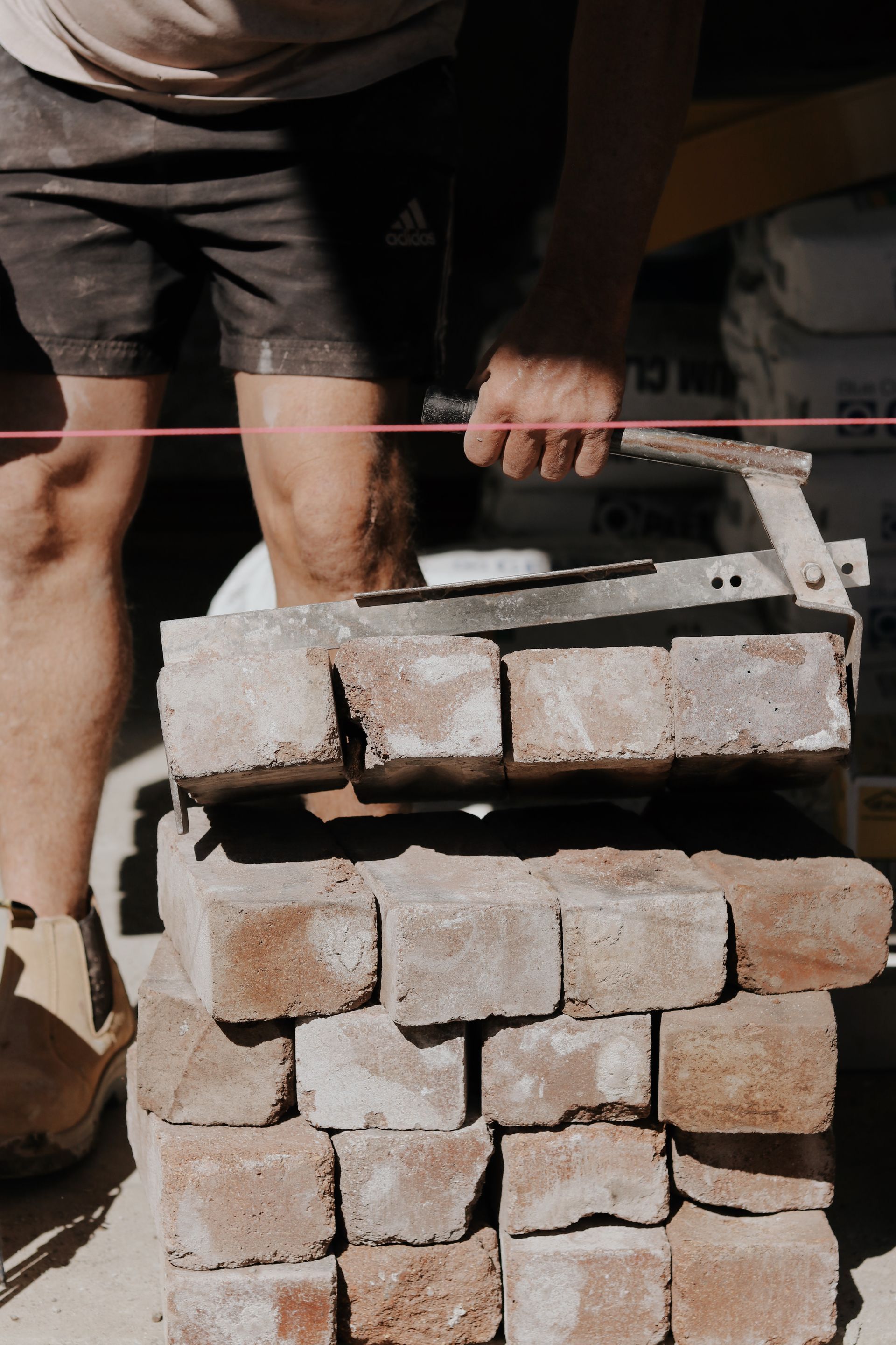 Person lifting a stack of paving stones with a mechanical gripper outdoors— Ryan's Bricklaying In Eleebana, NSW