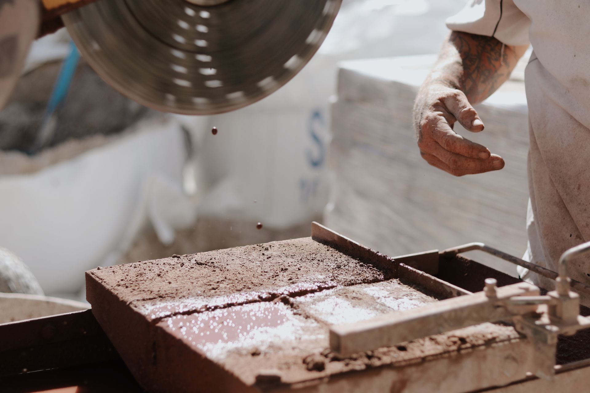Circular saw cutting a brick, dropping liquid. Hands in gloves, white sacks in the background— Ryan's Bricklaying In Eleebana, NSW
