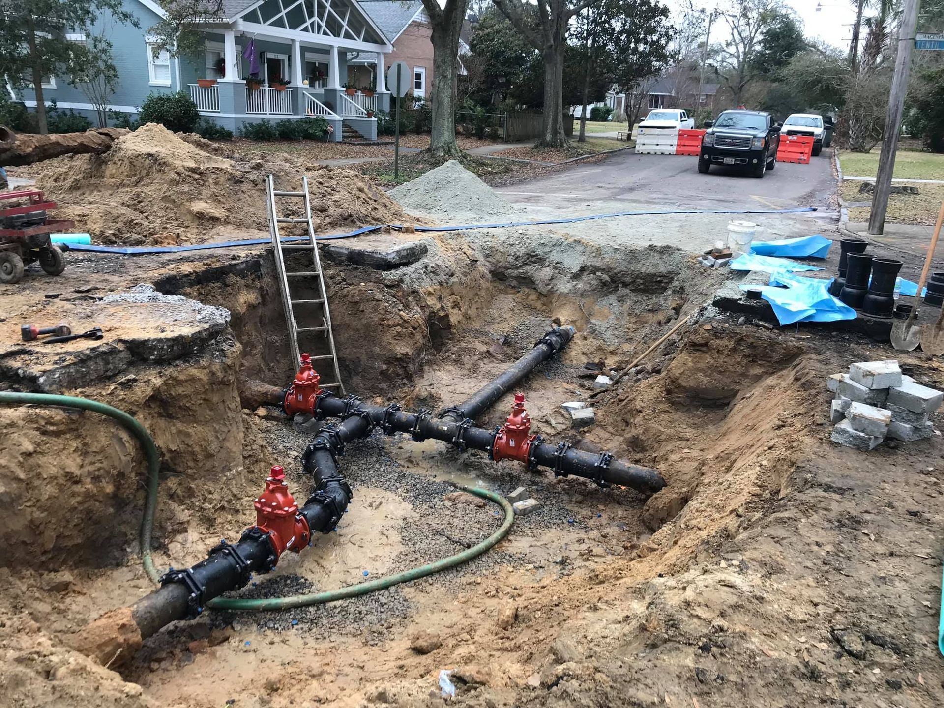 Water pipes exposed in a construction pit, with valves and a ladder in a residential street.