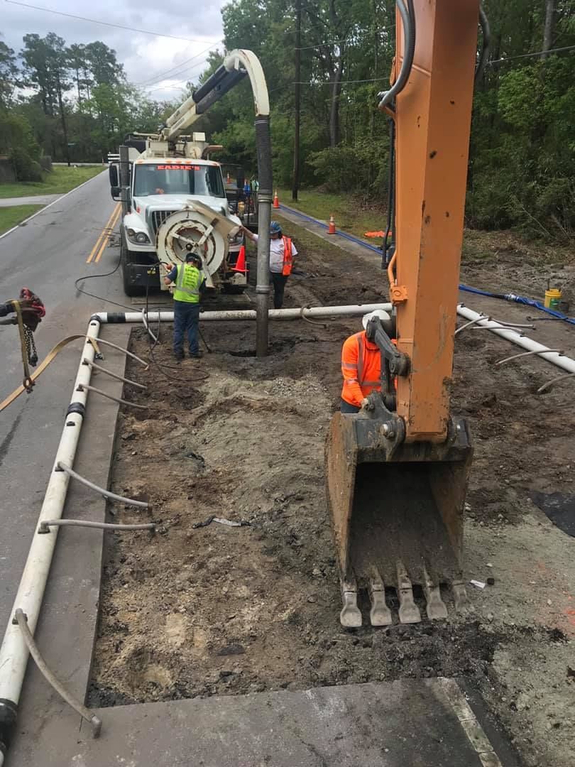 Road construction: Workers use an excavator and vacuum truck to dig a trench in a paved road.