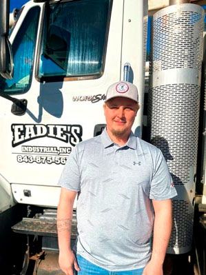 Man in grey shirt and cap stands in front of a truck with 