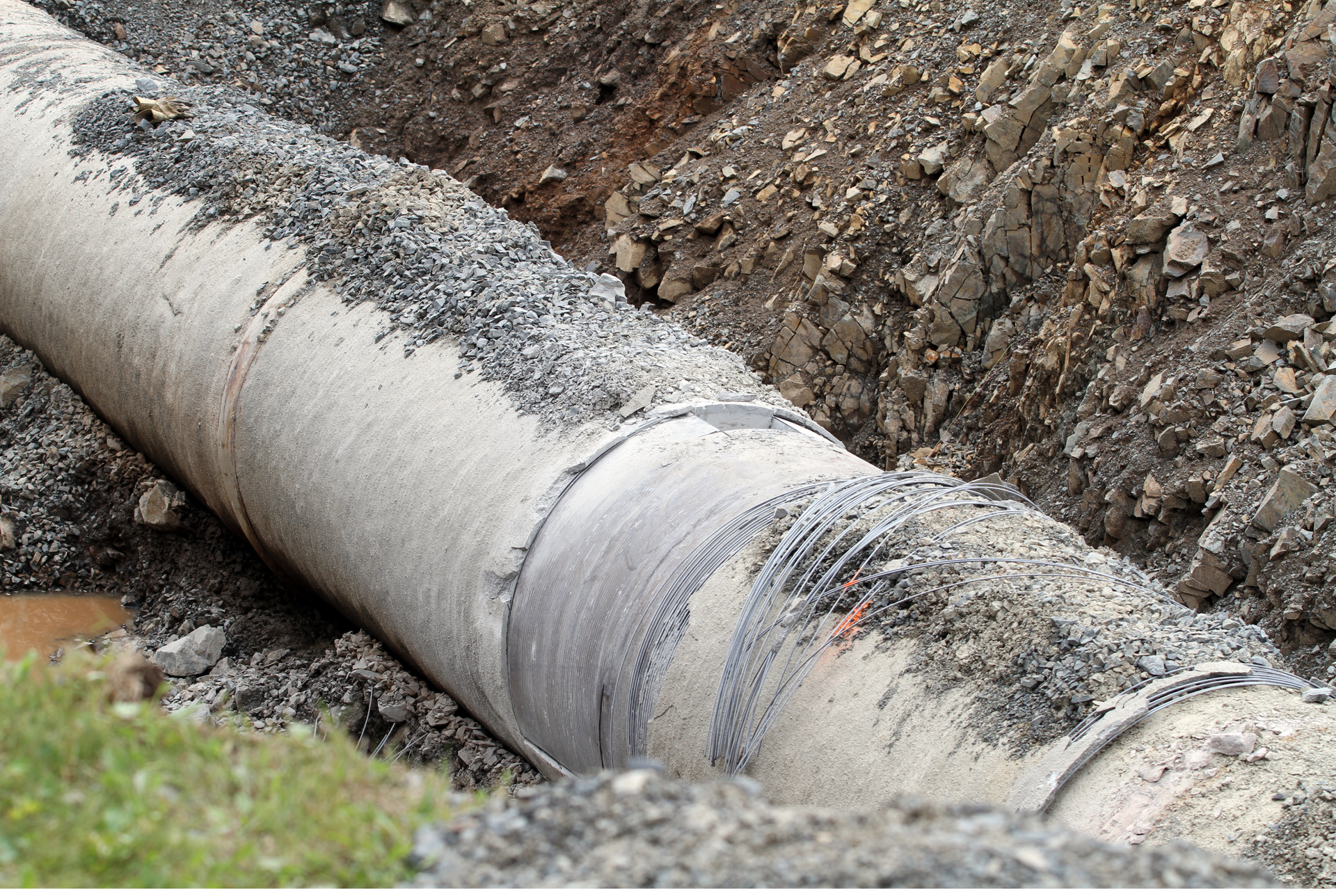 Large, gray pipe in an earthen trench, partially covered in dirt and gravel.