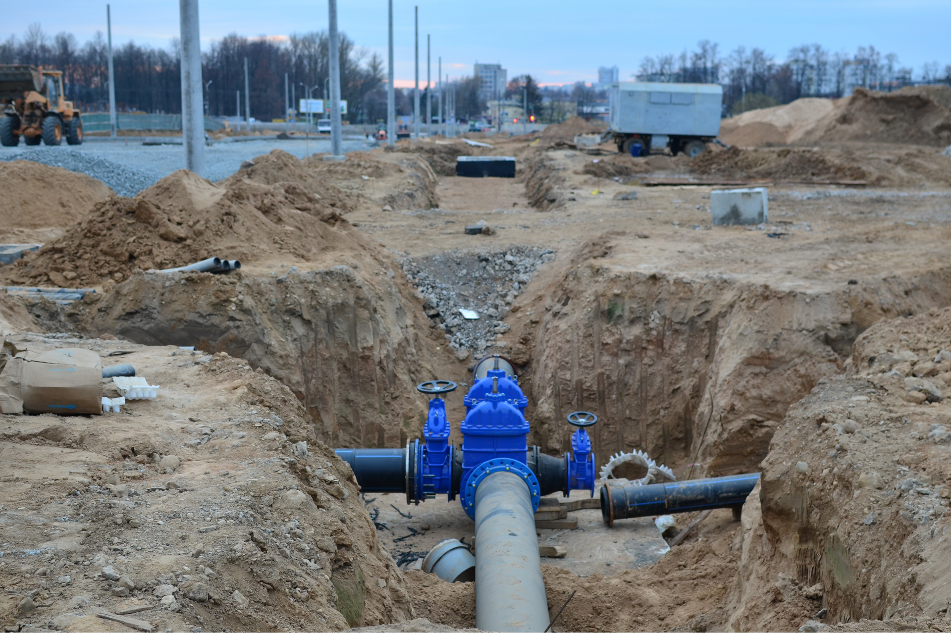 A construction site with exposed water pipes and blue valves in a trench.