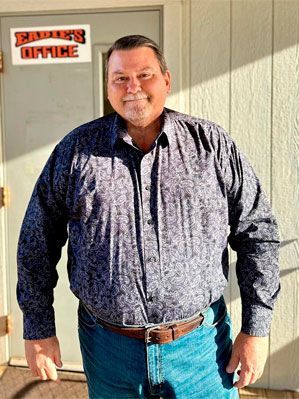 Man in patterned shirt and jeans, standing outside an office marked 