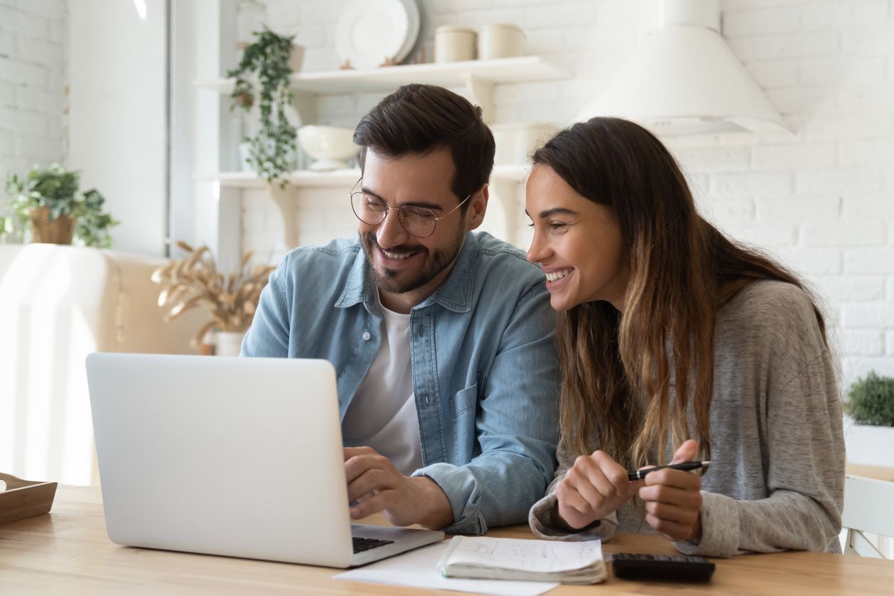 A man and a woman are sitting at a table looking at a laptop computer.