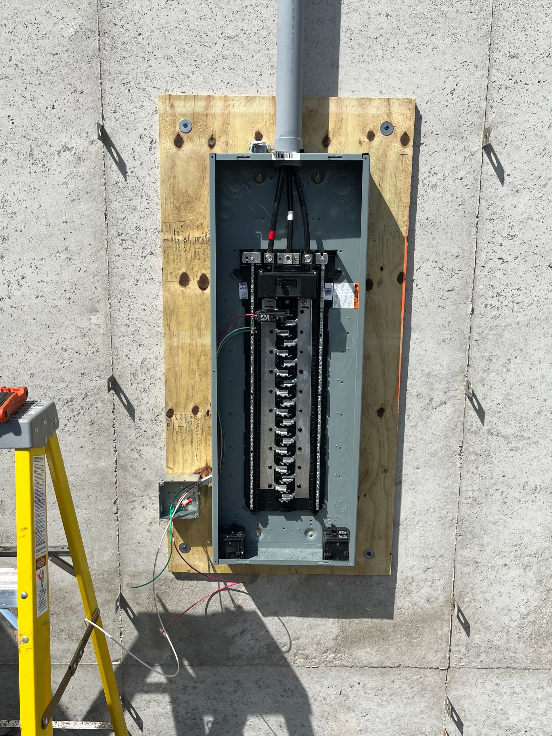 A ladder is sitting next to an electrical box on a concrete wall installed by Patriot Electrical Solutions.