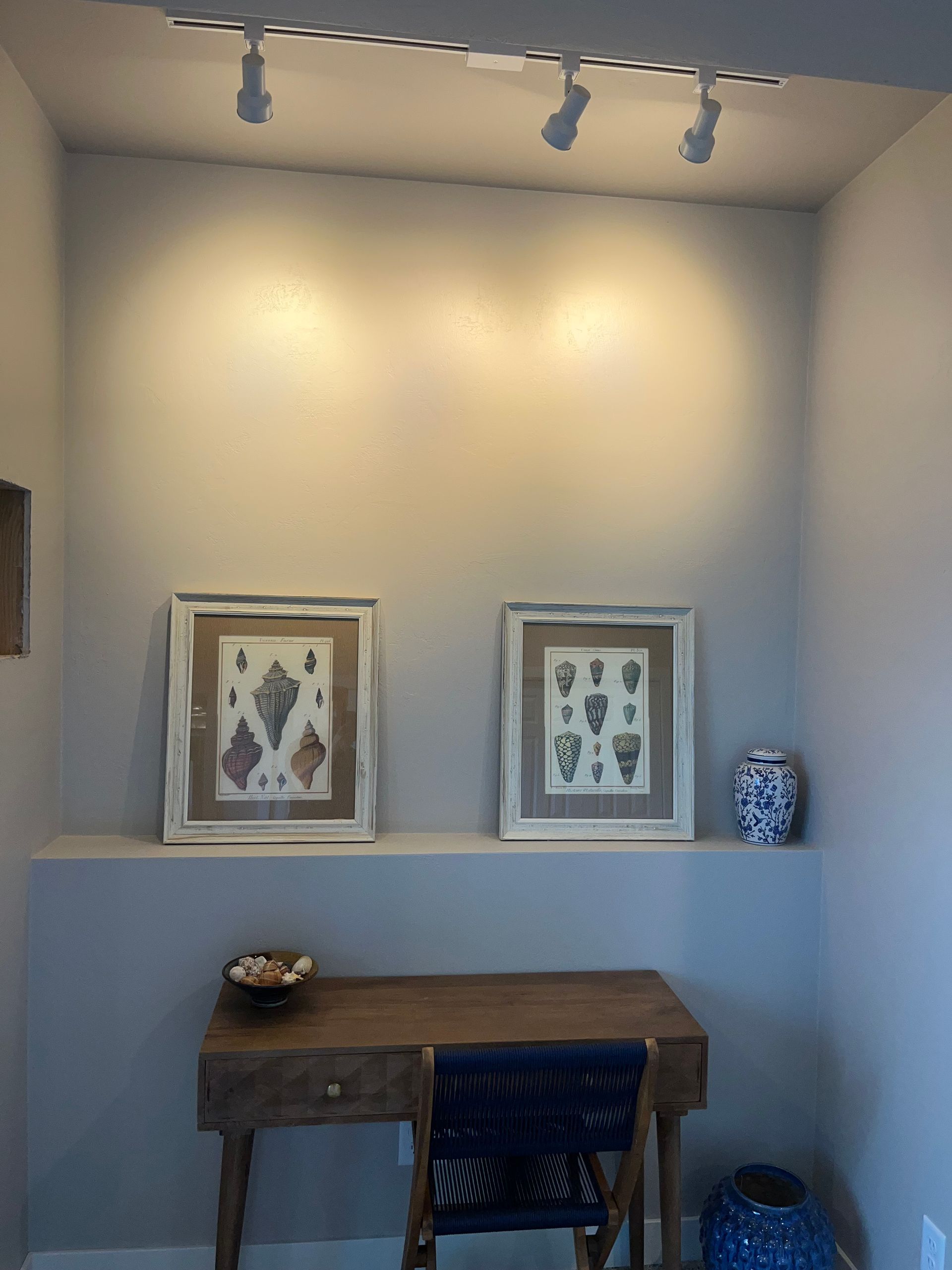 A room with a desk , chair , and two pictures on the wall.