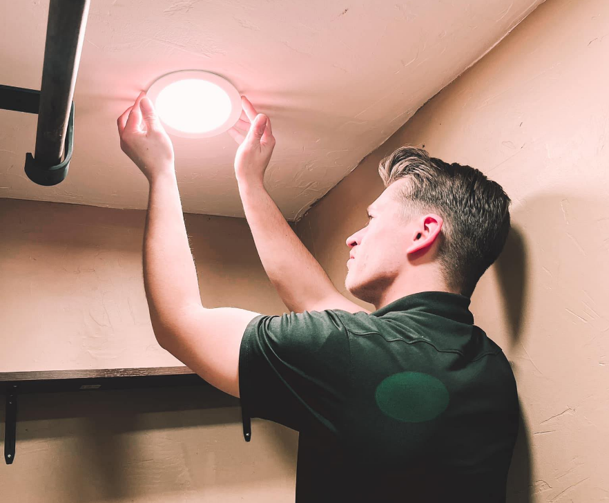 A Patriot Electrical Solutions technician is fixing a light on the ceiling of a room.