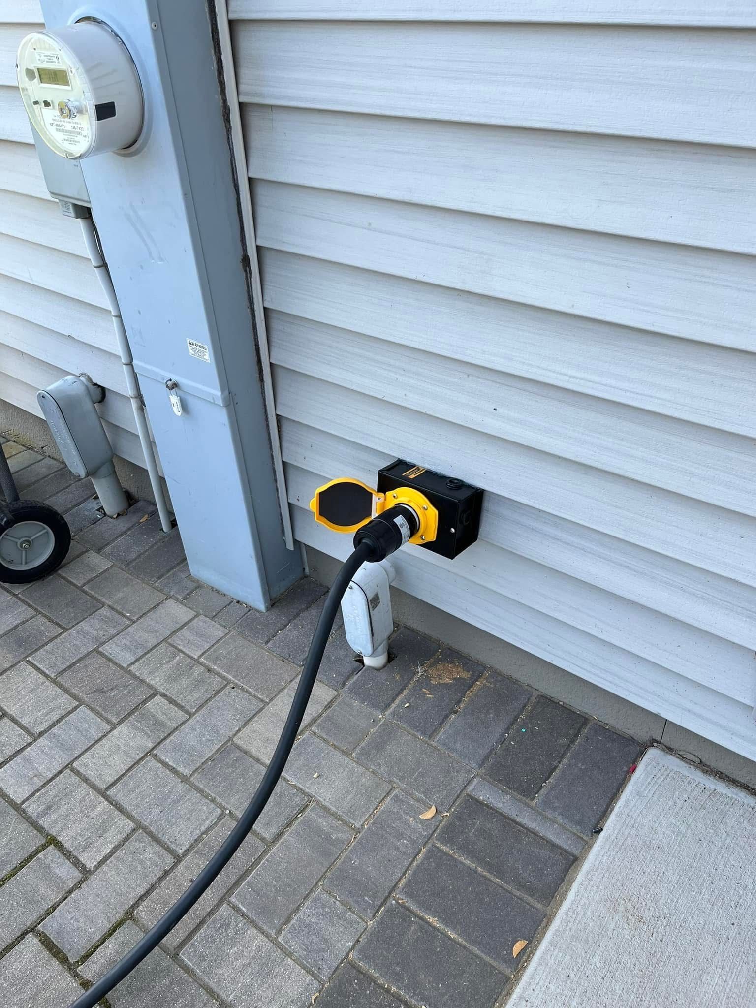 A hose is plugged into a power outlet on the side of a building installed by Patriot Electrical Solutions.