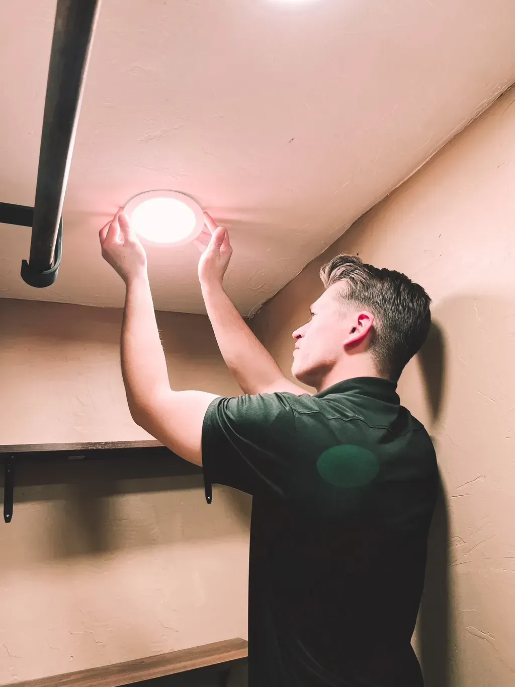 A Patriot Electrical Solutions technician is installing a light on the ceiling of a room.