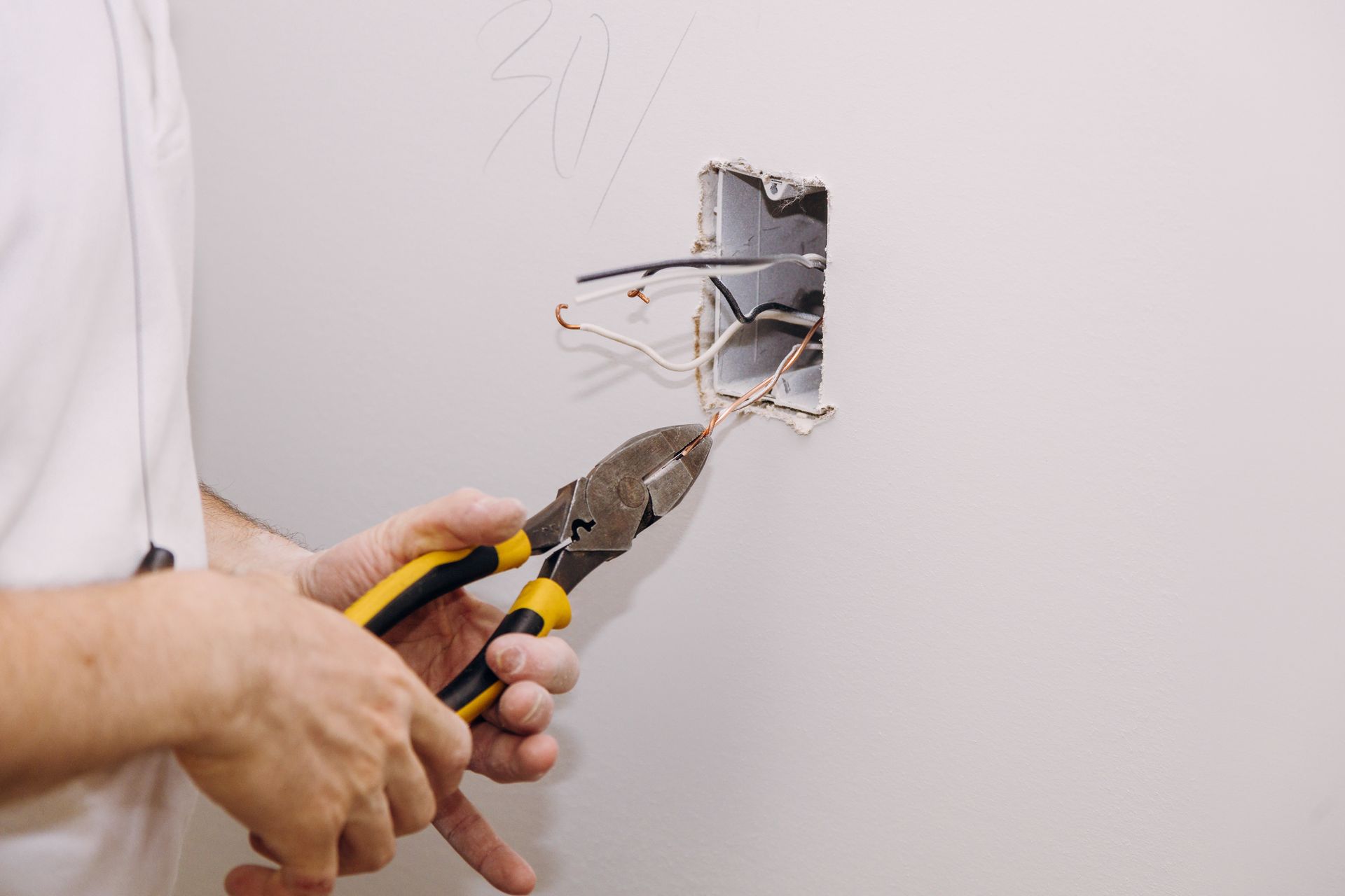 A person using pliers to cut electrical wires inside a wall outlet during repair work