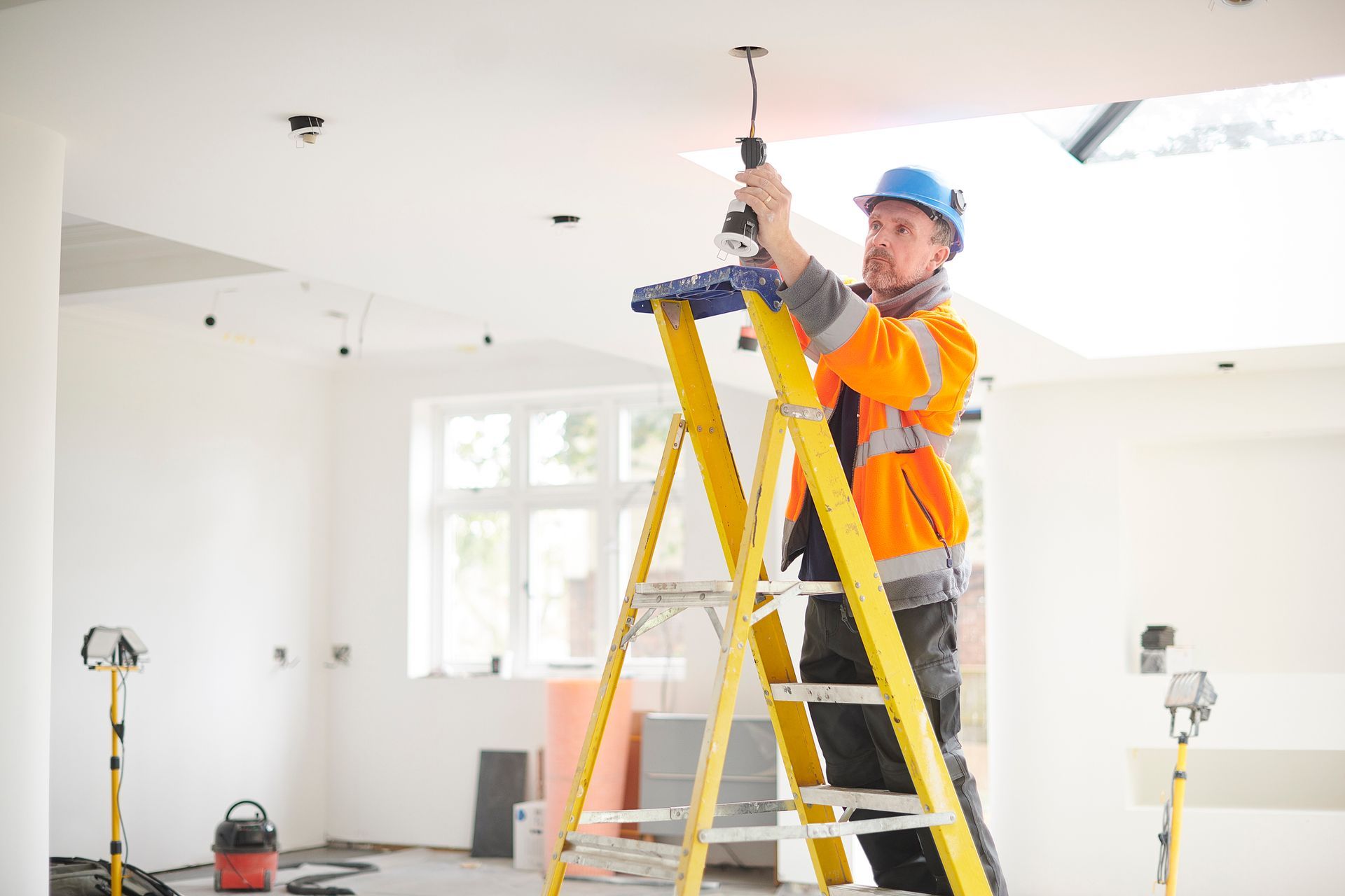 A man is standing on a ladder working on a light fixture.