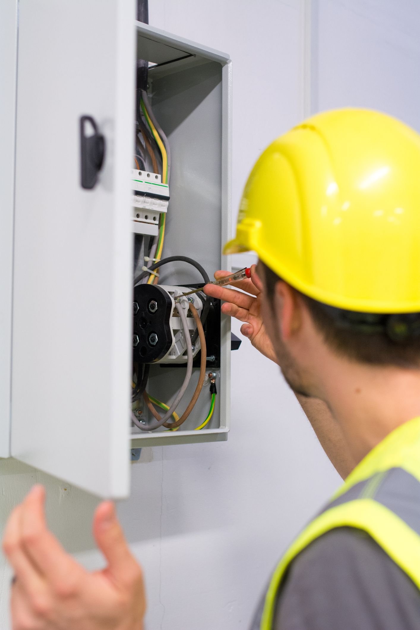 A man wearing a yellow hard hat is working on an electrical box.