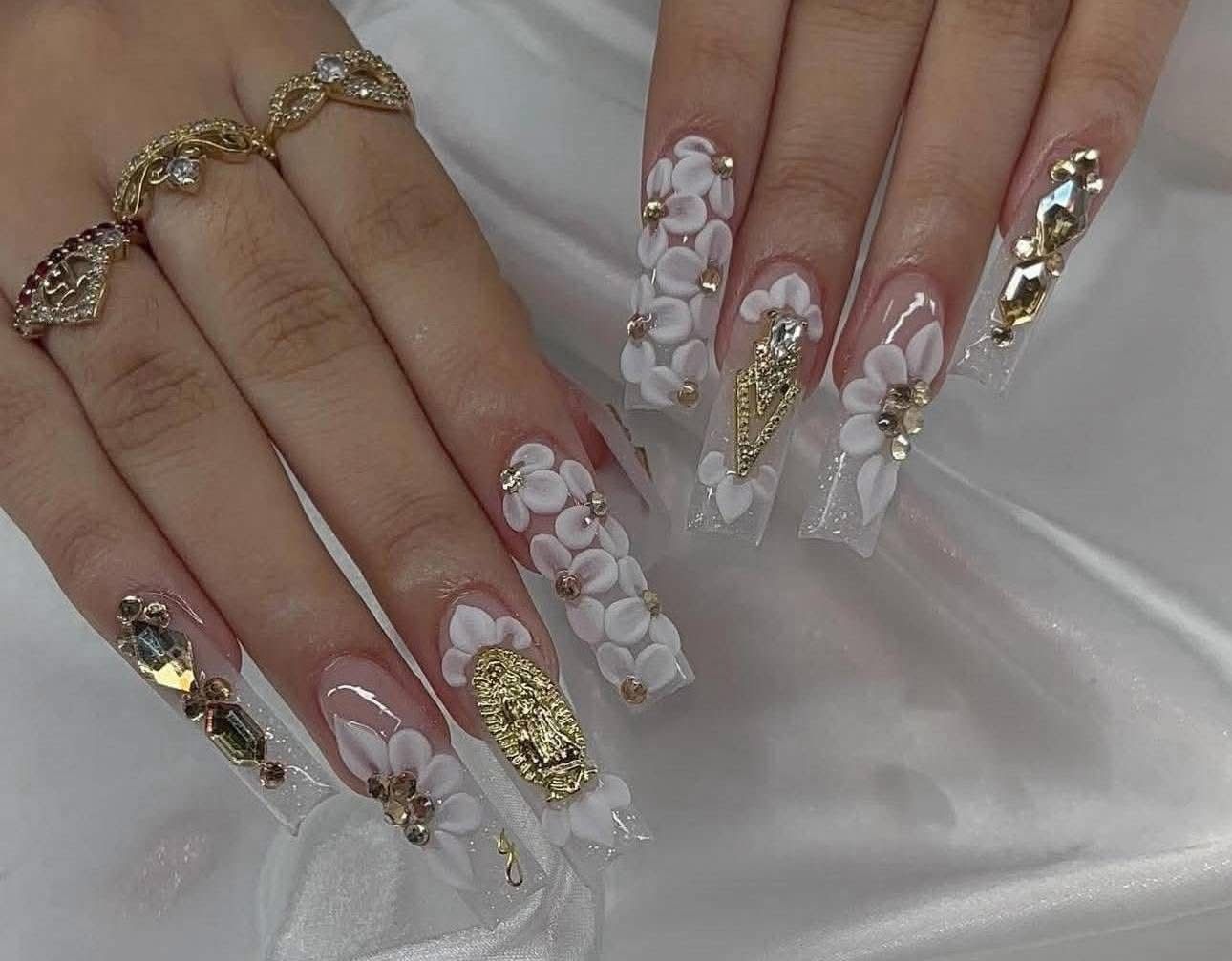 A woman 's nails are decorated with white and gold flowers and rhinestones