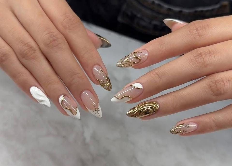 A close up of a woman 's nails with gold and white designs
