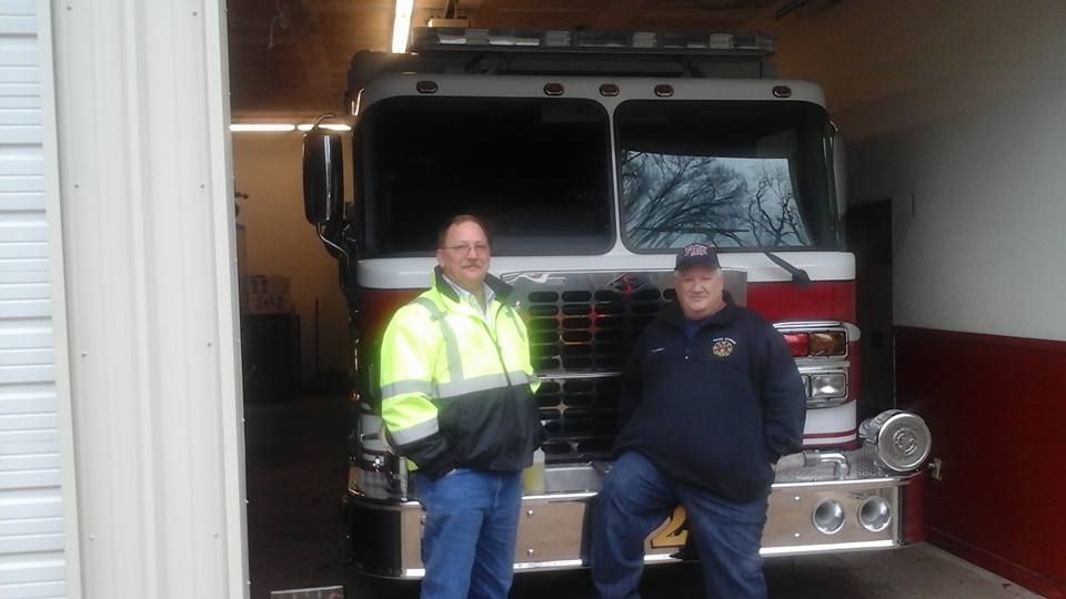 Two men are standing in front of a fire truck.